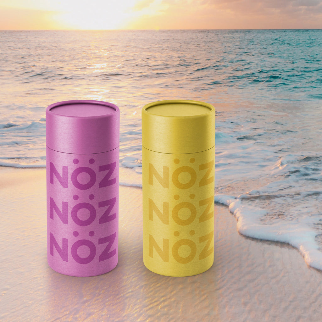 Nöz reef safe SPF sunscreen in pink and green on a beach.