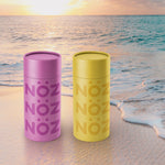 Load image into Gallery viewer, Nöz reef safe SPF sunscreen in pink and green on a beach.
